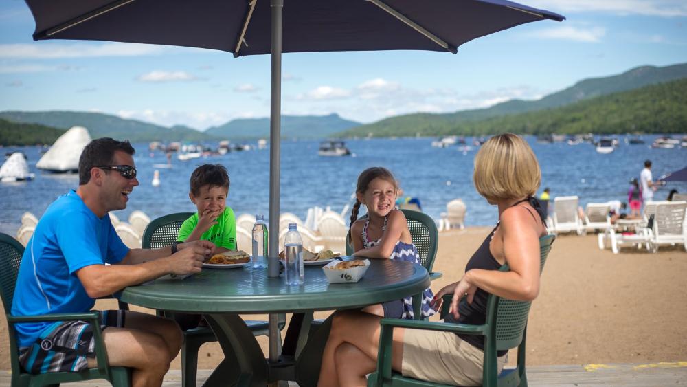 Adultes autour d'une table sous un parasol, club plage et tennis, lac Tremblant, Mont-Tremblant